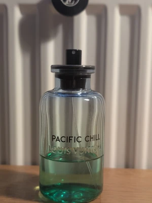 Louis Vuitton Pacific Chill parfym - Snygg parfymflaska från Louis Vuitton med namnet Pacific Chill. Flaskan är genomskinlig med en blågrön vätska och har en svart spraykork. Designen är stilren och modern, perfekt för dig som gillar exklusiva dofter och lyxiga detaljer. C 35 ml kvar 
