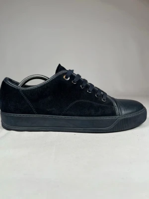 Svarta Lanvin skor i mocka och skinn - Stilrena svarta sneakers med ovandel i mocka och tåparti i skinn. Klassisk låg modell med rund tå och snörning. Passar perfekt till en clean och avslappnad look.