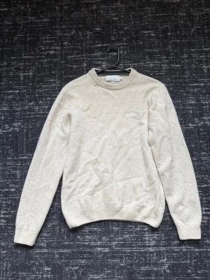 Beige stickad tröja  - Klassisk beige stickad tröja med rund halsringning och ribbade muddar vid ärmslut och nederkant. Tröjan har en enkel och stilren design som passar till det mesta, perfekt för kyligare dagar.