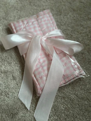 Rutig rosa quiltad handväska med rosett - Supersöt handväska i quiltad design med rosa och vitt rutigt mönster. Väskan har en dekorativ rosett framtill och insidan är fodrad med ett gulligt tryck. Perfekt för dig som gillar en söt och romantisk stil. Cute for Organizing your makeup and other accessories