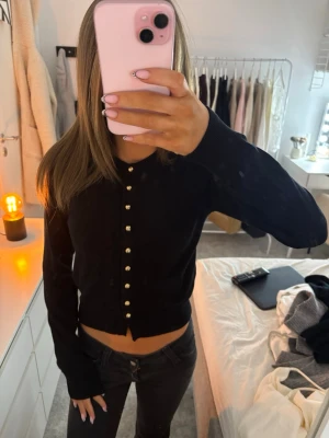 Svart kofta med guldknappar - Säljer en svart kofta med snygga guldknappar framtill. Modellen är croppad och har långa ärmar med ribbade muddar. 