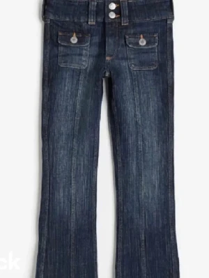 Mörkblå bootcut jeans med fickor - Snygga mörkblå jeans med bootcut passform och markerade sömmar. Jeansen har två framfickor med lock och knappdetaljer samt dubbla knappar i midjan. Perfekta för dig som gillar en klassisk men trendig look.