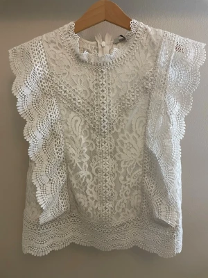 Vit spetsblus från ONLY XS - Supersöt vit blus från ONLY i storlek XS, helt täckt av detaljerad spets med blommönster. Blusen har korta, volangprydda ärmar och mittemellan hög hals med fina spetskanter. 
