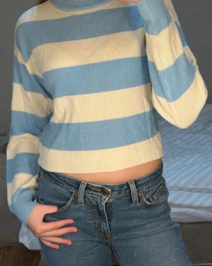 Blåvit randig stickad tröja - Säljer en croppad stickad tröja med breda blå och vita ränder. Tröjan har långa ärmar, ribbad struktur och en avslappnad passform. Perfekt för dig som gillar en chill och trendig stil.