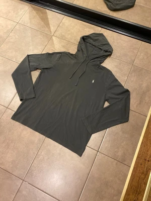 Ralph Lauren Lightweight Hoodie - Snygg mörkgrå tunn hoodie från Polo Ralph Lauren. Grå färg med vit logga på bröstet. Perfekt för en avslappnad och stilren look. Postar inom 24 h📦