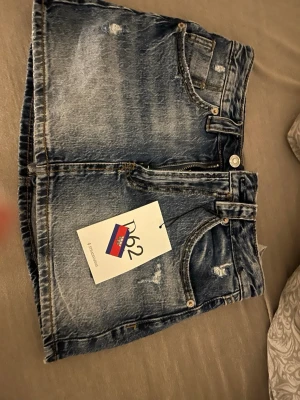 Blå jeanskjol från Stradivarius - Trendig blå jeanskjol från Stradivarius i kort modell med regular waist. Har inbyggda shorts och just denna färgen säljs inte längre.