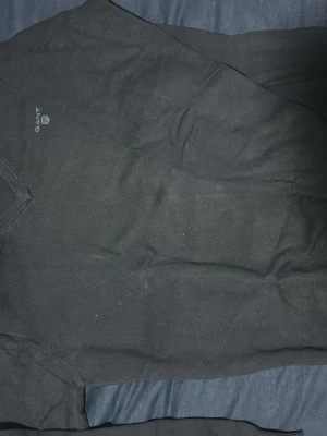 Svart V-ringad tröja från Gant - Klassisk svart V-ringad tröja från Gant med diskret logga broderad på bröstet. Tröjan har långa ärmar och ribbade muddar vid ärmslut och nederkant. Perfekt att bära över en skjorta för en stilren look.