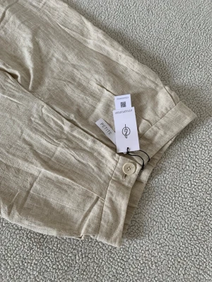 Stradivarius beiga linnebyxor från Stradivarius - Snygga beige linnebyxor från Stradivarius i modellen Petite. Byxorna har raka ben, hög midja och stängs med knapp framtill. Perfekta för en chill och stilren look under varma dagar. Storlek 38 men är snarare som en 36 / S !
