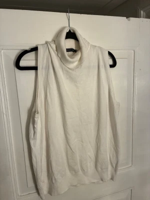 Vit polotopp från STOCKH LM - Säljer en vit ärmlös polotopp från STOCKH LM. Toppen har en hög, ribbad polokrage och är tillverkad i ett mjukt, stickat material. Perfekt att styla lager på lager eller bära som den är för en clean look. Passar M/L.