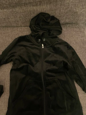 Svart velourhoodie från Gina Tricot - Mjuk och skön svart hoodie i velour från Gina Tricot. Hoodien har dragkedja framtill, två fickor och en stor huva med snörning. Perfekt för en avslappnad och trendig look.