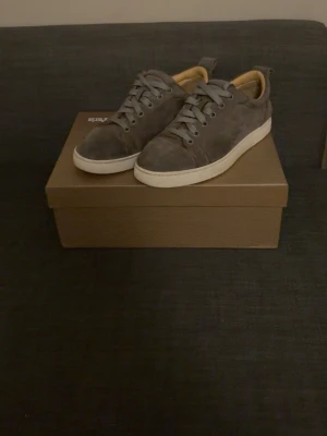 Grå mockasneakers med röd sula - Snygga grå sneakers i mocka med vita sulor och den ikoniska röda sulan. Skorna har klassisk snörning och en stilren, rund tå. Insidan är beige vilket ger en schysst kontrast. Perfekta för dig som gillar en clean och modern look. Skriv vid funderingar.