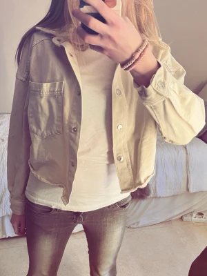 Beige croppad jeansjacka - Snygg beige croppad jeansjacka med klassisk krage. Jackan har knappar framtill och långa ärmar. Perfekt till sommaren. Säljer då den är för liten. Väldigt bra skick 💕