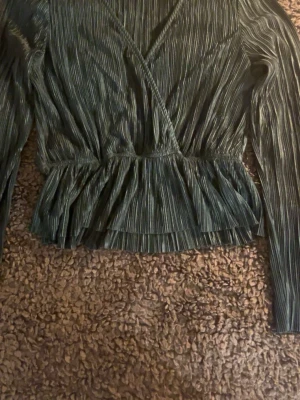 Grön omlottopp från Gina Tricot - Jätte fin mörkgrön omlottopp från Gina Tricot med plisserat typ och volang nedtill. Toppen har långa ärmar och v-ringad halsringning, perfa för dig som tycker om trendiga toppar💕