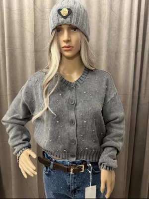 Grå kofta med pärldetaljer - Trendig grå kofta med rund halsringning och stora knappar framtill. Koftan är dekorerad med små pärlor över hela plagget och har ribbade muddar vid ärmslut och nederkant. Perfekt för dig som gillar en stilren men ändå unik look.