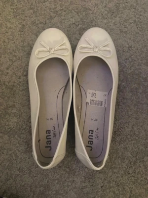 Vita ballerinaskor (37) - Snygga vita ballerinaskor från Jana med rund tå och dekorativ rosett framtill. Skorna har en klassisk och enkel design med platt sula. Skorna är använda en gång.