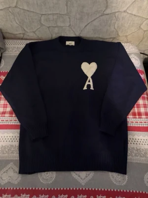 Ami Paris  - Snygg mörkblå stickad tröja från Ami med ett vitt hjärta och bokstaven A broderat på bröstet. Tröjan har rund halsringning, ribbade muddar och är gjord i mjukt stickat material. Perfekt för dig som gillar stilrena detaljer. Helt ny storlek m