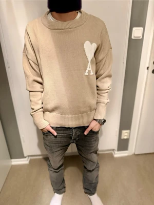 Beige stickad tröja från Ami Paris - Snygg beige stickad tröja från Ami Paris med stort vitt hjärta och A-logga på bröstet. 