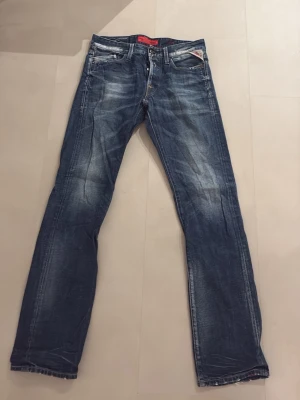 Blå Replay Grover jeans straight fit - Säljer ett par blå Replay Grover jeans med klassisk straight fit och slitna detaljer. Jeansen har fem fickor, normal midja och tydliga kontrastsömmar. Materialet är robust denim i bomull och passformen är avslappnad men ändå snygg. 29w 32L