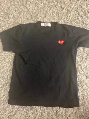 Svart Comme des Garçons PLAY t-shirt - Svart t-shirt från Comme des Garçons PLAY med det ikoniska röda hjärte-logotypen broderad på bröstet. Klassisk passform med rund hals och korta ärmar. Perfekt basplagg med en stilren och trendig touch.