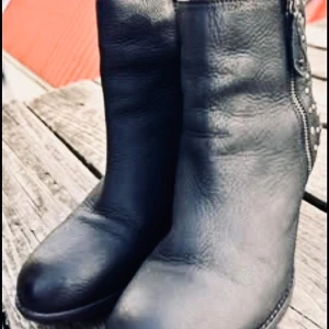 Rockiga stövletter från Mary B! - Fina rockiga svarta stövletter från Mary B i storlek 39 med dekorativa detaljer och dragkedja på insidan. Klacken i trä är ca 5 cm hög och dom är nyputsade och impregnerade.