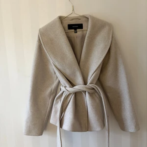 Beige omlottjacka från Vero Moda - Snygg beige omlottjacka från Vero Moda med bred krage och knytband i midjan. Jackan har lång ärm och är tillverkad i mjukt ullblandat material. Jackan är enbart använd fåtalet gånger så den är i mycket bra skick!🩷🫧✨🐆