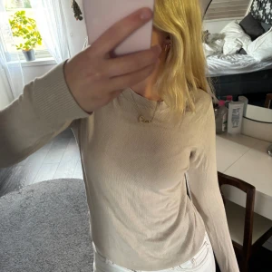 Beige långärmad tröja i bomull - Säljer en stilren beige långärmad tröja med rund halsringning. Tröjan är i mjuk bomull och har ribbade muddar vid ärmslut och nederkant. Perfekt att matcha med jeans eller kjol för en clean look.