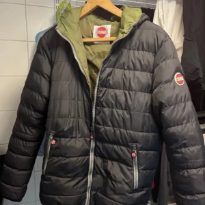 Svart pufferjacka från Colmar - Snygg svart pufferjacka från Colmar med en grön insida och huva. Jackan har en dragkedja framtill och två fickor med dragkedjor. Perfekt nu till våren då den är lite tunnare. Passar perfekt på mig som är 185 men köpte när jag va 180 så märker ingen skillnad. Priset är inte hugget i sten så kom med bud jag tar första bästa pris