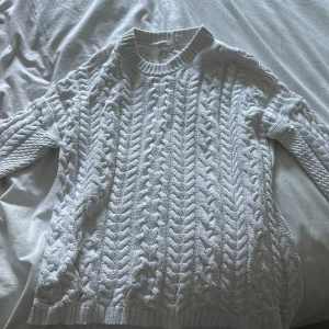 Vit kabelstickad tröja - Kabelstickad vit tröja med grov struktur och ribbade muddar vid hals, ärmslut och nederkant. Tröjan har en klassisk rund halsringning och lång ärm, perfekt för lager-på-lager under kyliga dagar. Perfekt nu inför hösten och väldigt bekväm! inga defekter eller liknande
