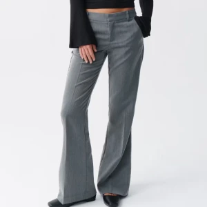 Grå kostymbyxor med bootcut - Snygga grå kostymbyxor med bootcut och låg midja. Byxorna har klassiska pressveck, hällor för bälte och stängs med dragkedja och knapp. Perfekta för en clean och stilren look. Materialet är slätt och känns dressat.