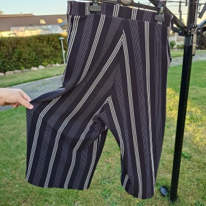 Svarta randiga wide byxor - Säljer ett par svarta byxor med vita vertikala ränder. Byxorna har en bred och luftig passform med croppad längd, perfekt för dig som gillar en chill och trendig stil. Resår i midjan för extra komfort. Materialet känns mjukt och följsamt.
