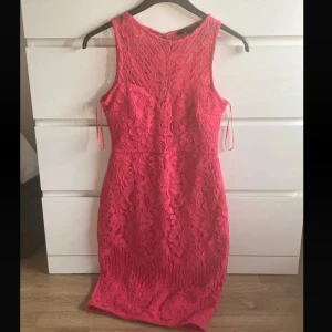 Rosa spetsklänning från Lipsy London - Supersnygg rosa spetsklänning från Lipsy London i figurnära modell. Klänningen är ärmlös, har rund halsringning och vackert blommigt spetsmönster över hela plagget. Slits bak och dragkedja i ryggen. Perfekt för dig som vill sticka ut!