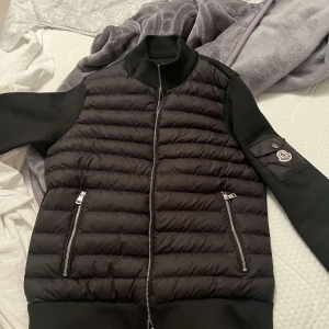  Moncler - Svart pufferjacka från Moncler med quiltad front, släta ärmar och Moncler-logga på ärmficka. Priset kan gå ner lite i snabb affär 