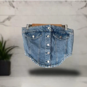 Ljusblå jeanstopp  från Perfect Jeans - Supersnygg ljusblå jeanstopp från Perfect Jeans med knappar framtill och två fejkade fickor med lock. Toppen har en cool, lite rundad nederkant och klassiska jeanssömmar. Perfekt för dig som gillar denim och vill sticka ut lite extra.