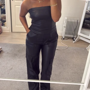 Cargojumpsuit  i skinnimitation - Säljer denna jumpsuit i skinnimitation och cargofickor. Använd 1 gång. Köpt från Zara. Storlek 36-38. Pris 400 kr