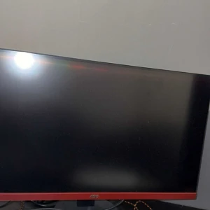 AOC Gaming Monitor - AOC gaming monitor med röd detalj, stor skärm och tunn ram. Skärmen är  i gott skick utan synliga repor eller skador. Perfekt för spel och arbete. Levereras med strömkabel och fot. Snygg design som passar alla skrivbord.