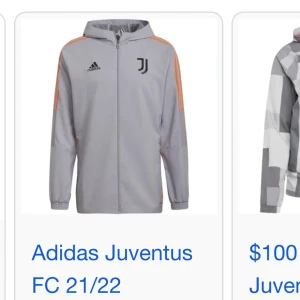 Grå Adidas Juventus hoddie - Snygg grå vindjacka från Adidas x Juventus med huva och hel dragkedja. Jackan har orange detaljer längs axlarna och Juventus-logga på bröstet. Perfekt för dig som gillar sportig stil och vill visa vilket lag du hejar på.