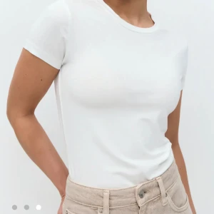 Vit basic t-shirt i bomull - Enkel och stilren vit t-shirt med rund hals och korta ärmar. Modellen är figurnära och tillverkad i mjuk bomull som känns skön mot huden. Perfekt att matcha med jeans eller kjol för en clean look.