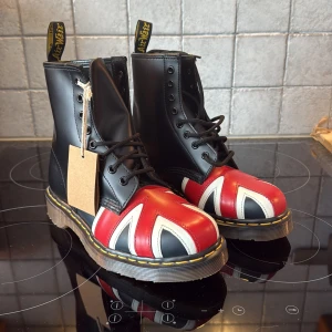 Dr. Martens boots med Union Jack - Säljer ett par ikoniska Dr. Martens boots i svart skinn med Union Jack-flagga i rött, vitt och blått. Skorna är helt oanvända med tag på och är i storlek 38 för tjejer. Skriv vid funderingar och annat.