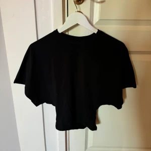 Svart topp från Nelly - Svart topp från Nelly i mjuk bomull. T-shirten har korta ärmar och en loose passform upptill med klassisk rund halsringning. Perfekt för en chill och avslappnad stil.