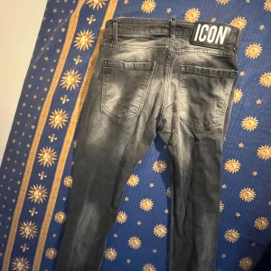 Svarta jeans med ICON-tryck - Snygga svarta jeans med slitna detaljer och coolt stort 'ICON'-tryck på ena benet. Jeansen har en tvättad look, vita färgstänk och patch med siffran 2. Klassisk femficksmodell och normal passform. Perfekta för dig som vill sticka ut med din stil.