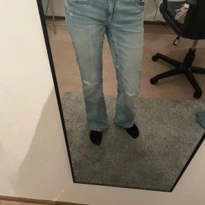 Ljusblå bootcut jeans Gina Tricot - Säljer ett par ljusblå jeans från Gina Tricot i bootcut-modell. Jeansen har klassisk femficksdesign, lätt slitna detaljer vid knäna och snygga bakfickor med knapp. Tillverkade i jeansmaterial och sitter skönt på kroppen.