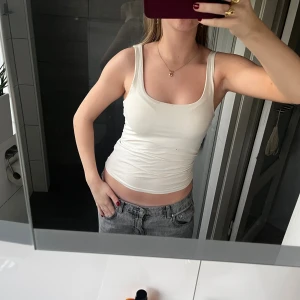 Vit ribbad linnetopp - Säljer en enkel och stilren vit linnetopp med breda axelband och rundad urringning. Toppen är ribbad och sitter tight mot kroppen, perfekt att matcha med jeans eller kjol. Materialet känns mjukt och stretchigt. Litet hål på framsidan av linnet, men ingenting som märks tydligt. 