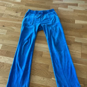 Blå velourbyxor Juicy Couture S - Blå mjukisbyxor från Juicy Couture i velour med bred resår och snörning i midjan. Byxorna har raka ben, stora fickor fram och bak med tryckknappar. Perfekta för en chill och trendig look. (Pris kan diskuteras) 