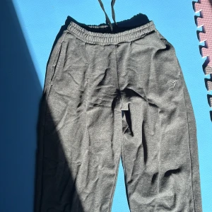 Grå mjukisbyxor från Gymshark XS - Mörkgrå mjukisbyxor från Gymshark i storlek XS. Joggers har elastisk midja med snörning, muddar vid bensluten och Gymshark-logga broderad på benet. Perfekta för chill eller träning, riktigt sköna och stilrena. Bra pumpcover och sköna att bära! Slutsålda på gymshark. Har även bruna och vita som säljs! Använda få gågner! Inköpspris 550!