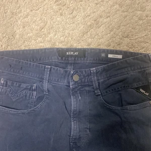 Blå Replay Anbass jeans, stl 31 - Snygga blå Replay Anbass jeans i klassisk femficksmodell. Jeansen har raka ben, normal passform och tydliga Replay-detaljer som logga på fickan och patch bak. Tillverkade i mjukt bomullsmaterial med en stilren look.