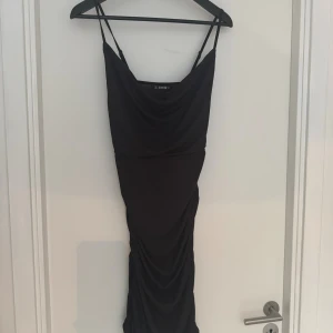 Svart ribbad långklänning från SHEIN - Svart långklänning från SHEIN med tunna axelband och draperad halsringning. Klänningen är ribbad och har rynkade detaljer längs sidorna för en snygg siluett. Perfekt för dig som gillar en stilren och trendig look.