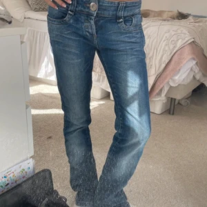 Lågmidjade booucut jeans - Snygga blå jeans från VILA med klassisk femficksdesign och coola broderade detaljer på bakfickorna. Jeansen har normal passform, utsvängda ben och är tillverkade i slitstarkt denim. Perfekta för dig som gillar en avslappnad men ändå trendig look. Midjemått 36 Innerbenslånhd 79