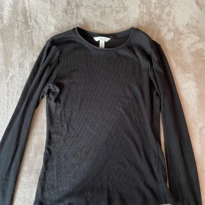 Svart ribbad långärmad tröja H&M - En svart, ribbad långärmad tröja från H&M. Tröjan har rund halsringning och är figurnära i modellen. Perfekt basplagg att styla med jeans eller kjol. Tillverkad i mjuk bomullsmix som är skön mot huden.