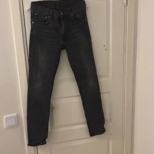 Nudie jeans w29 L32 - Snygga svarta jeans från Nudie Jeans med klassisk femficksdesign och diskreta slitningar. Jeansen har raka ben och normal passform, tillverkade i mjukt denimtyg. Perfekta för dig som gillar stilrena och tidlösa jeans med en cool vibe.