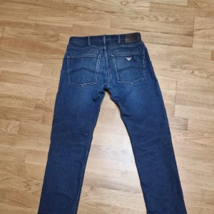 Armani Jeans blå denim byxor - Snygga blå jeans från Armani Jeans med klassisk femficksdesign och ikonisk logga på bakfickan. Jeansen har raka ben, normal passform och är tillverkade i slitstark denim. Perfekta för dig som gillar stilrena och tidlösa jeans med exklusiv känsla.